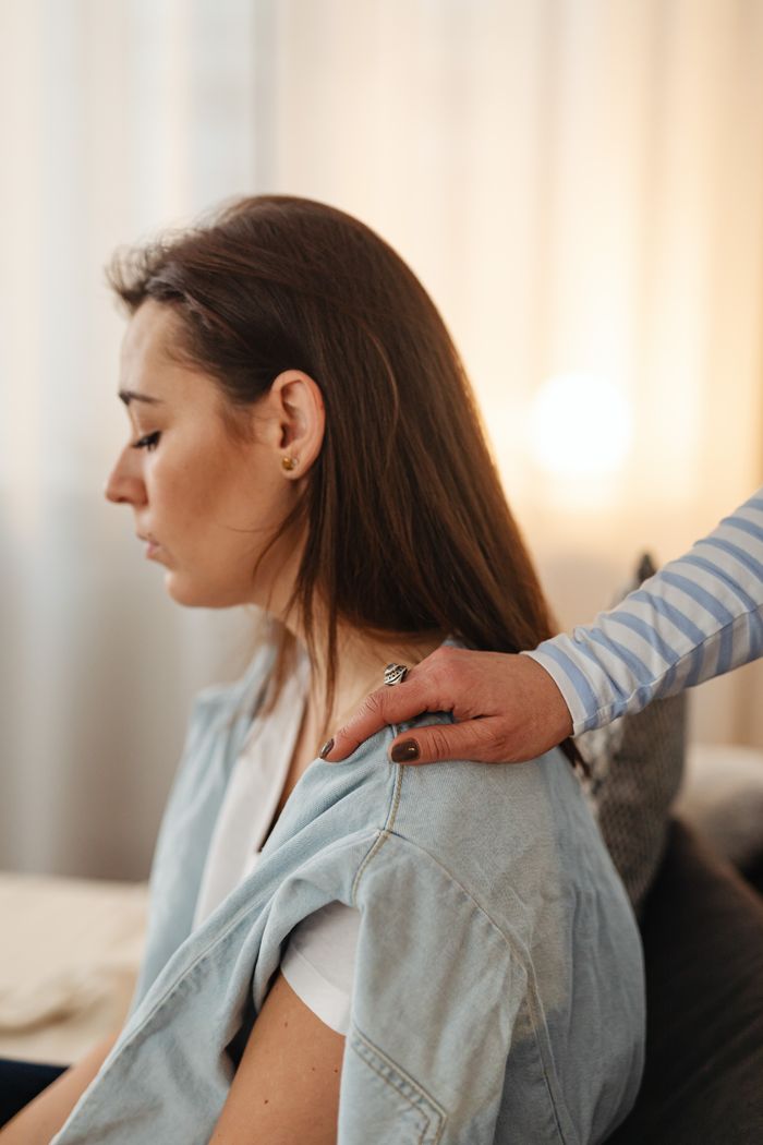 A close-up of a comforting touch on a woman's shoulder indoors, evoking empathy.