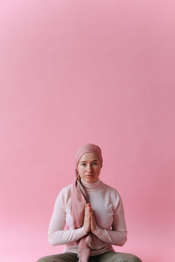 A woman in a headscarf sits gracefully, embodying hope and strength against a soft pink background.